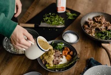 Person pouring sauce on plate full of meat and veggies