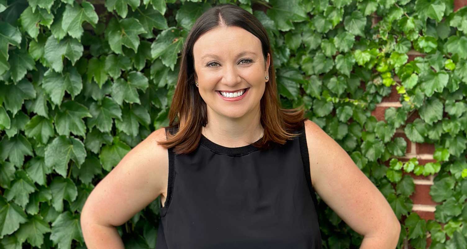 Stephanie Hoffman smiling at the camera with a wall of vines behind her