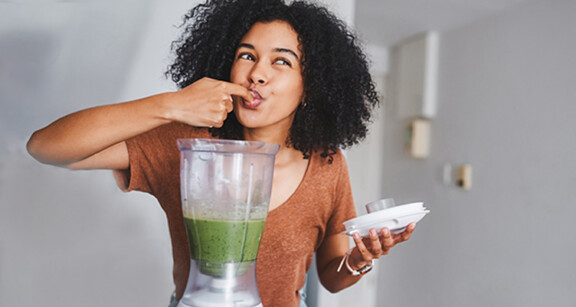 woman licking her finger after dipping it in a blender full of green smoothie