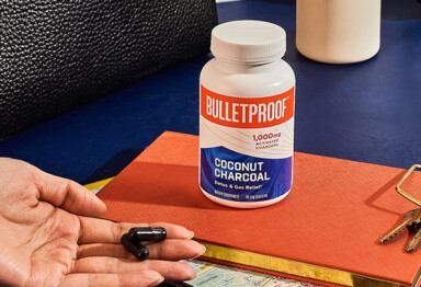 hand holds 3 coconut charcoal pills near a notebook and purse