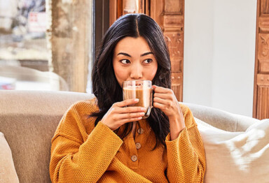 girl sits on couch in a yellow matching set drinking a mug of coffee