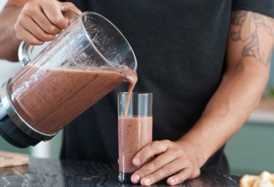 Man pouring protein shake into a cup from a blender.