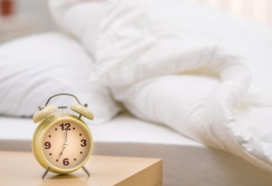 Yellow clock on nightstand next to white bed